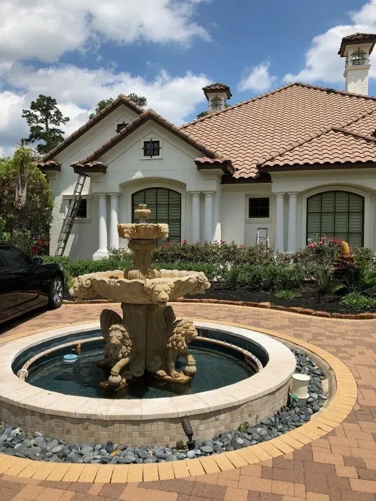Mediterranean-style house with a circular stone fountain in a landscaped front courtyard.