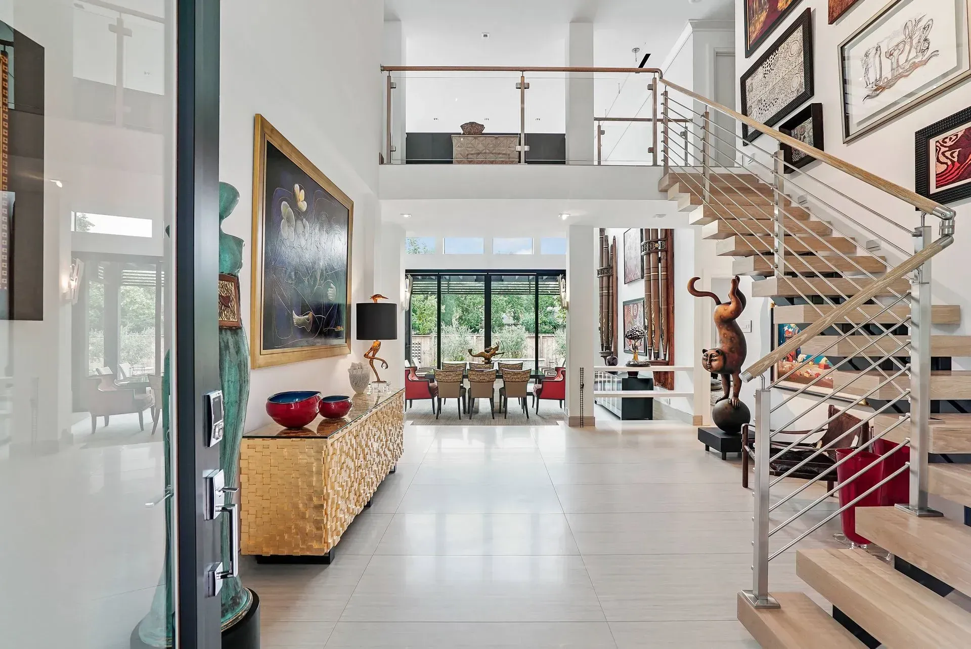 Bright modern foyer with white tile, staircase, artwork, and open living space beyond
