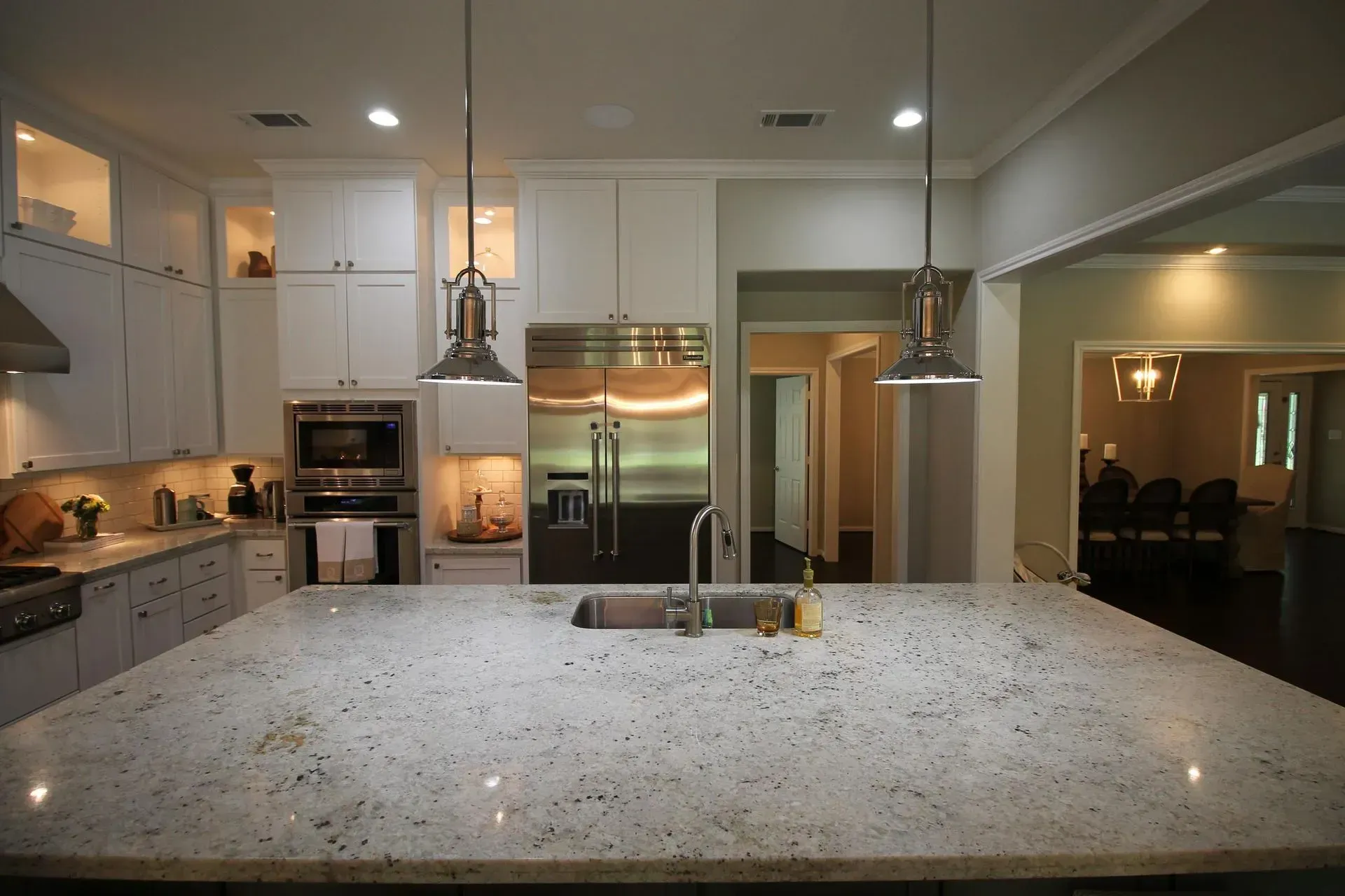 Modern kitchen with a large speckled island, white cabinets, and stainless steel appliances.