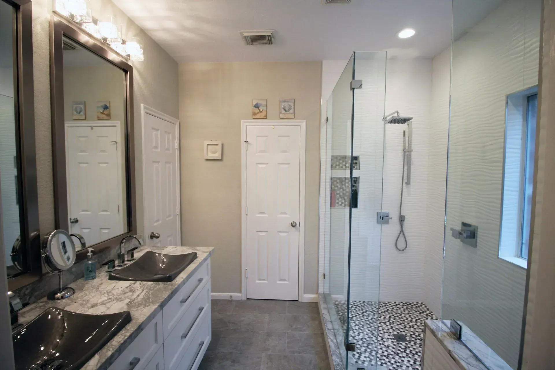 Bright modern bathroom with double vanity, large mirror, glass shower, and window.