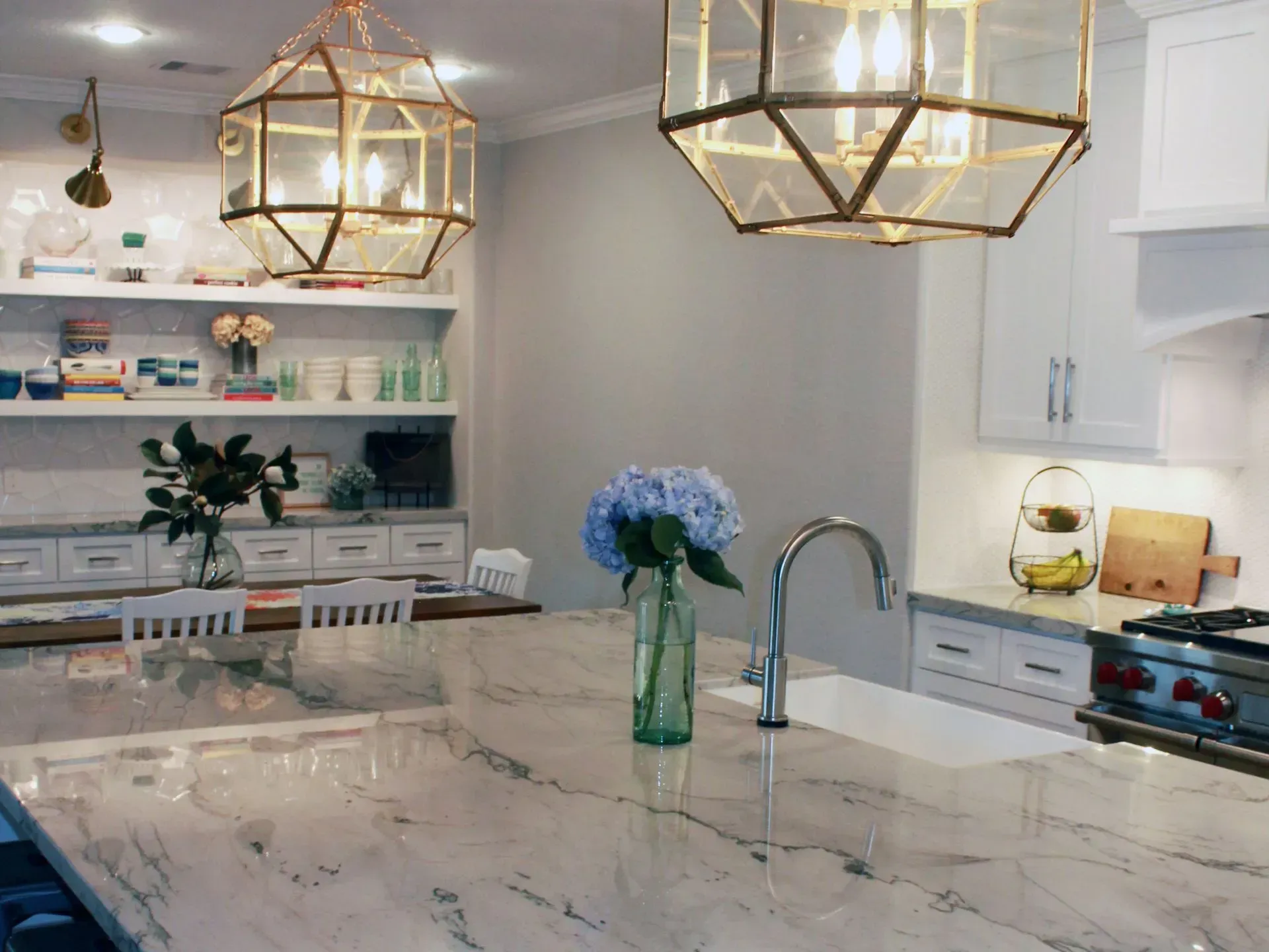Bright modern kitchen with marble island, brass pendant lights, and blue flowers in a vase