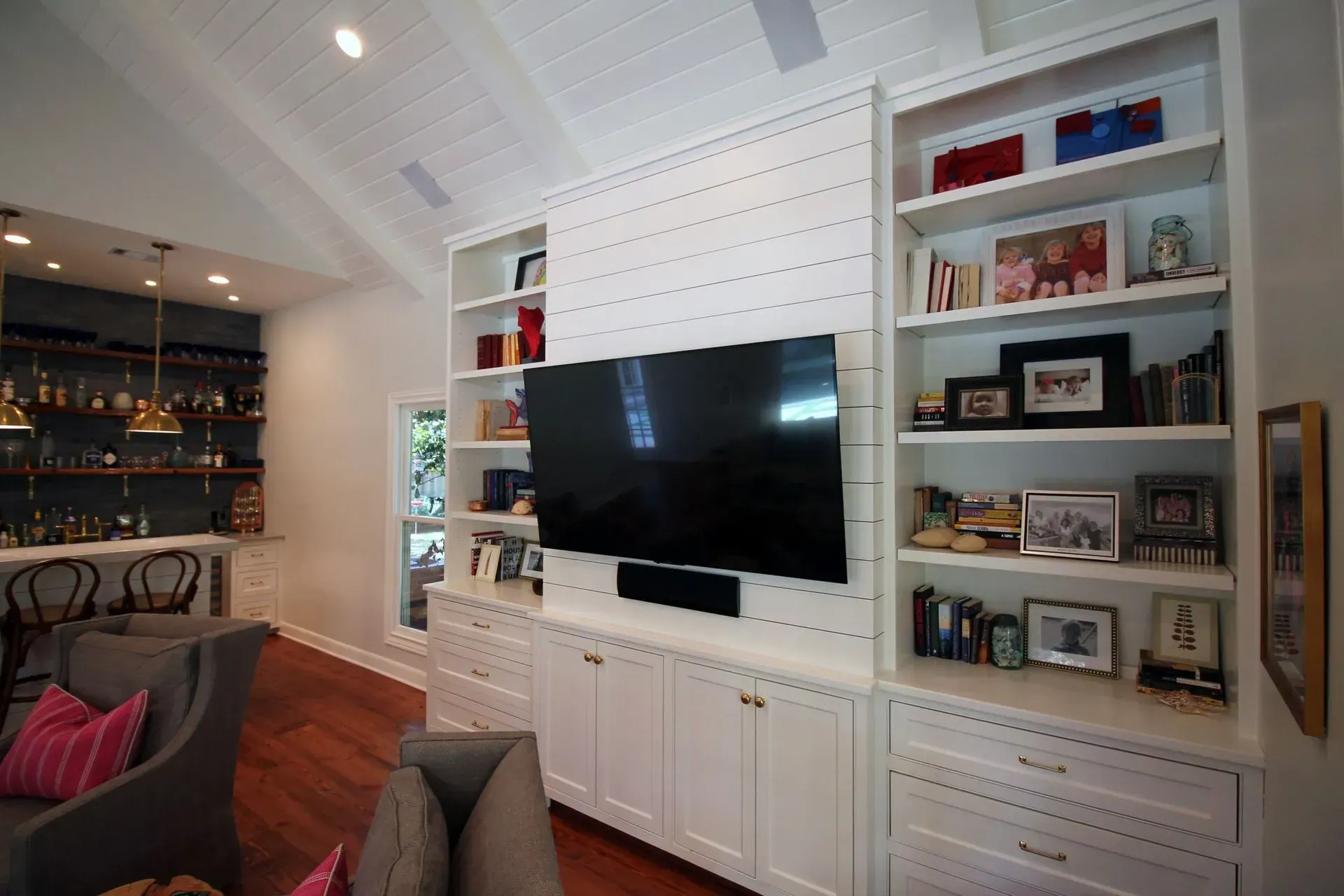 Living room with wall-mounted TV, white built-in shelves, and a dark bar area to the left.