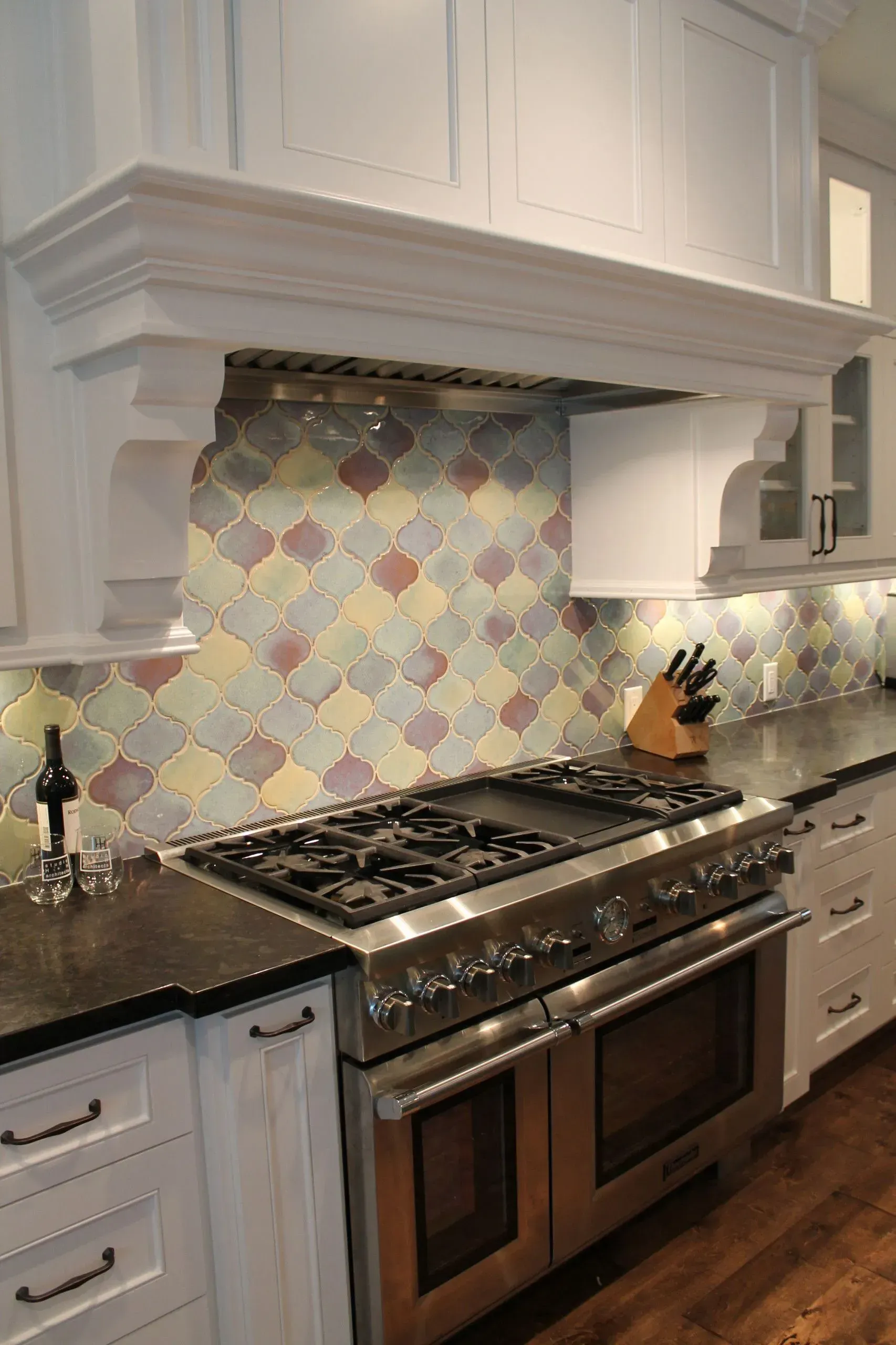 Bright kitchen with white cabinets, multicolored tile backsplash, and stainless steel gas range.