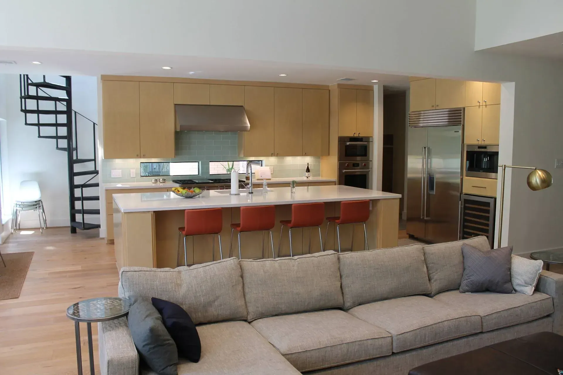 Open-plan living room and kitchen with a gray sofa, island stools, and stainless steel appliances