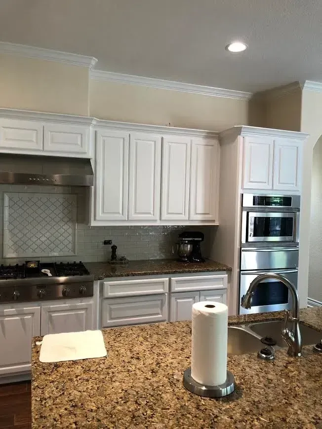 Bright kitchen with white cabinets, stainless appliances, and a granite island with paper towels.