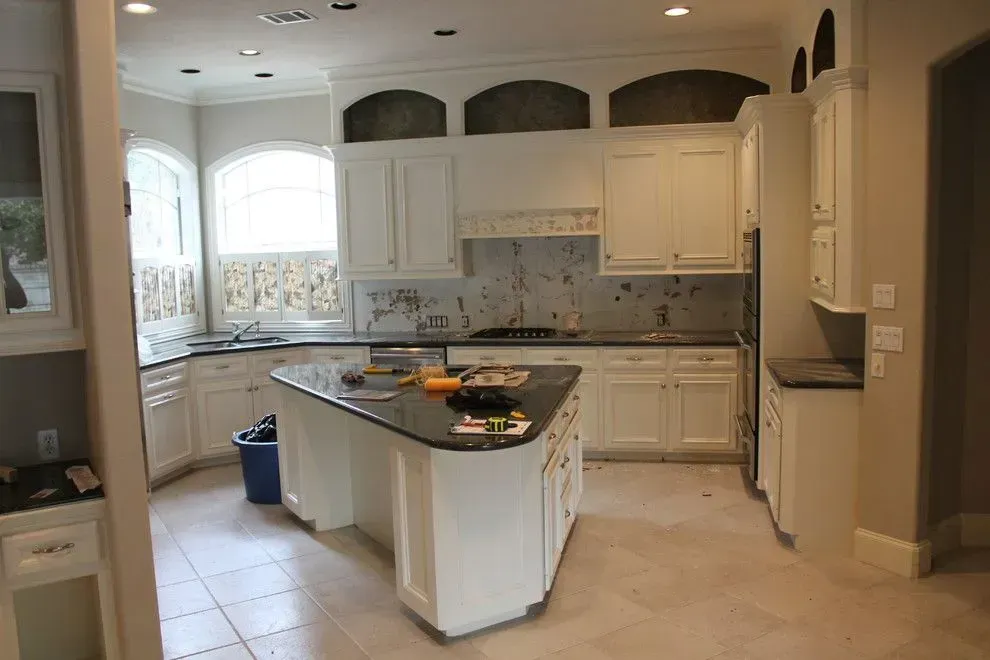 Bright white kitchen with island, black countertop, arched windows, and tiled floor