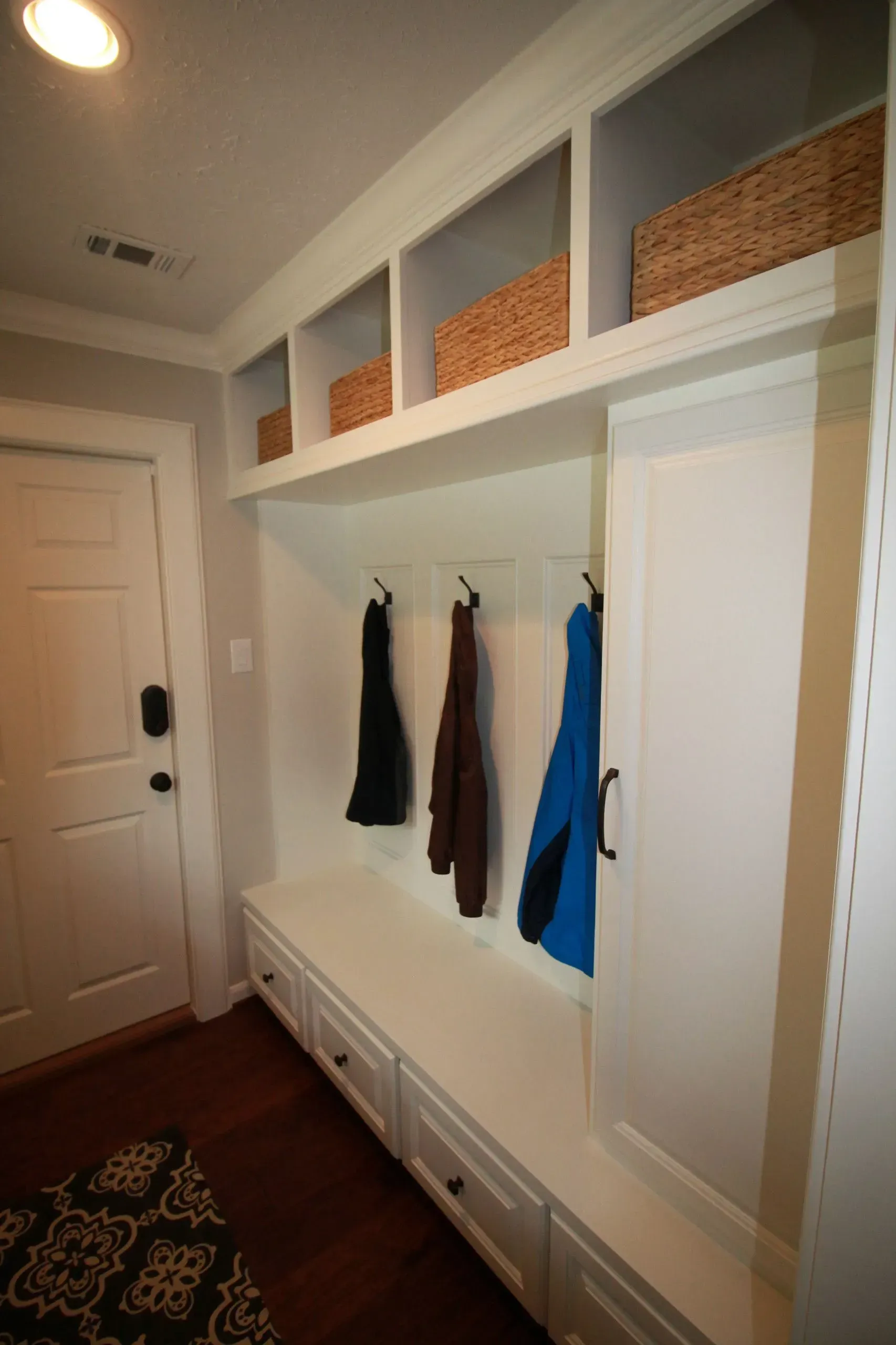 Built-in hallway storage with white cabinets, hanging hooks, and woven baskets above.