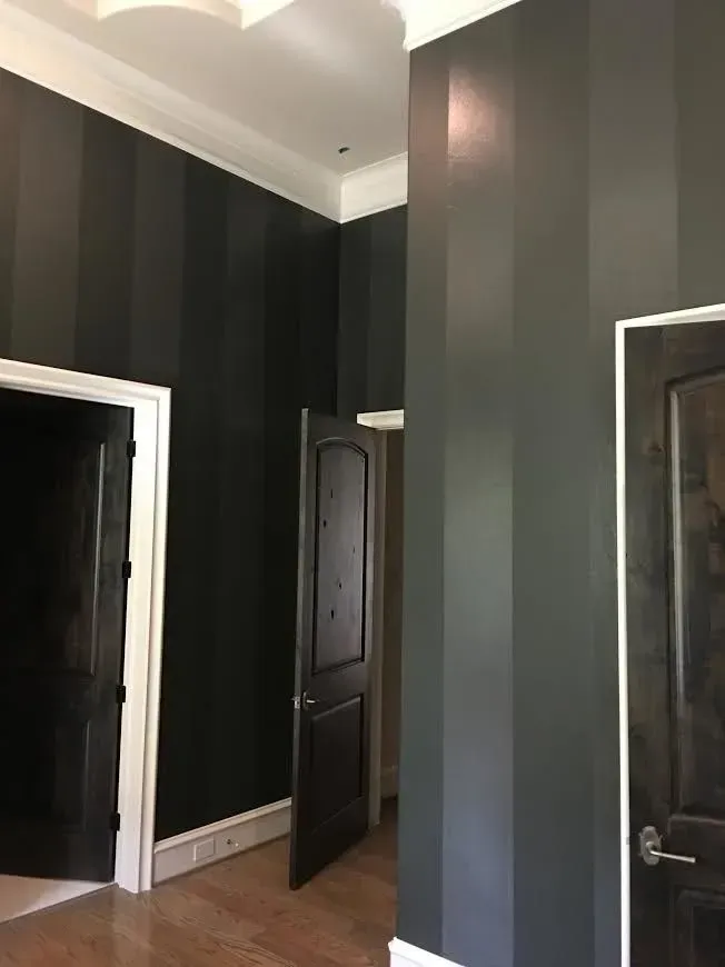 Hallway with dark striped walls, white trim, and two dark wood doors under a high ceiling.
