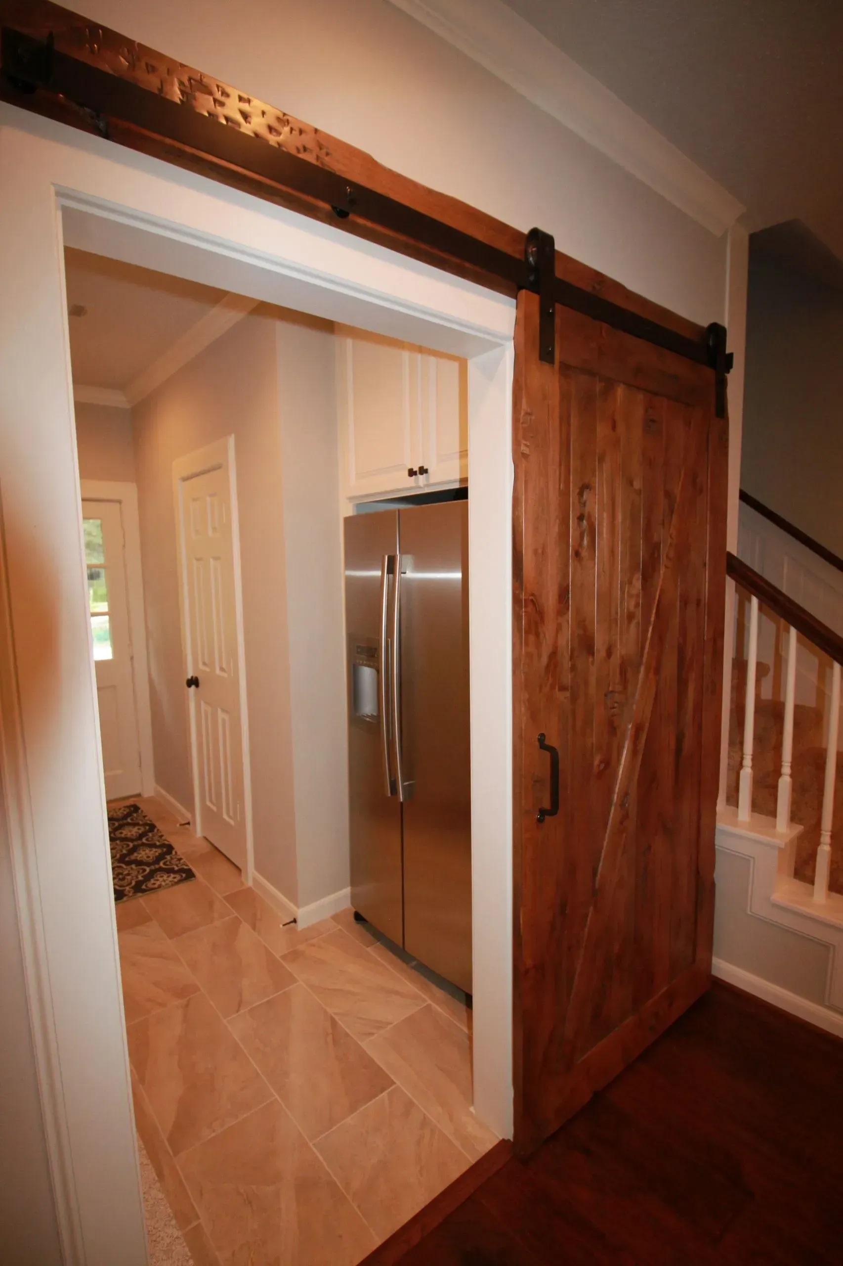Open wooden barn door reveals a kitchen hallway with stainless fridge and light wood floors.