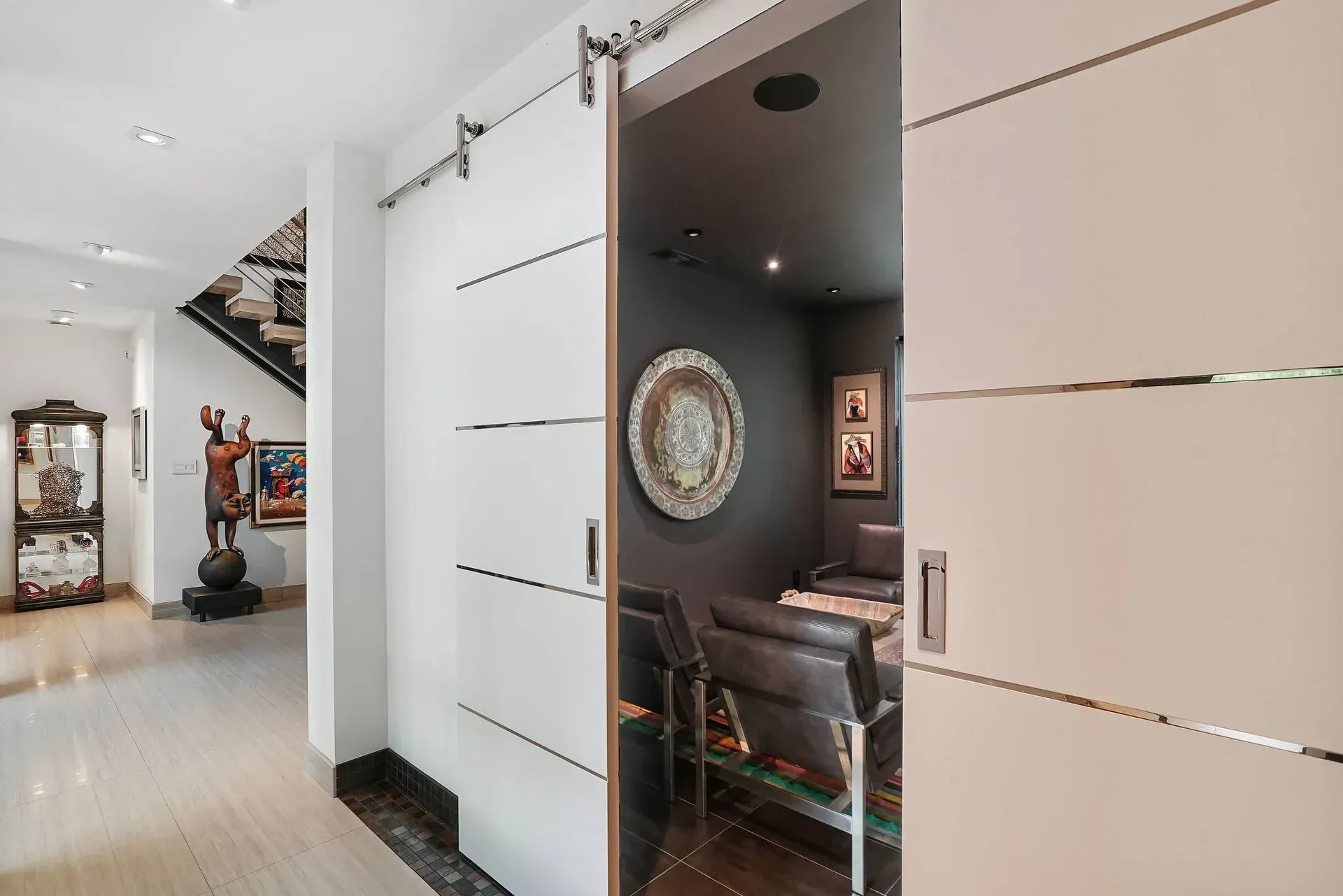 Modern hallway with white sliding doors open to a dark, cozy room with a mirror and chair