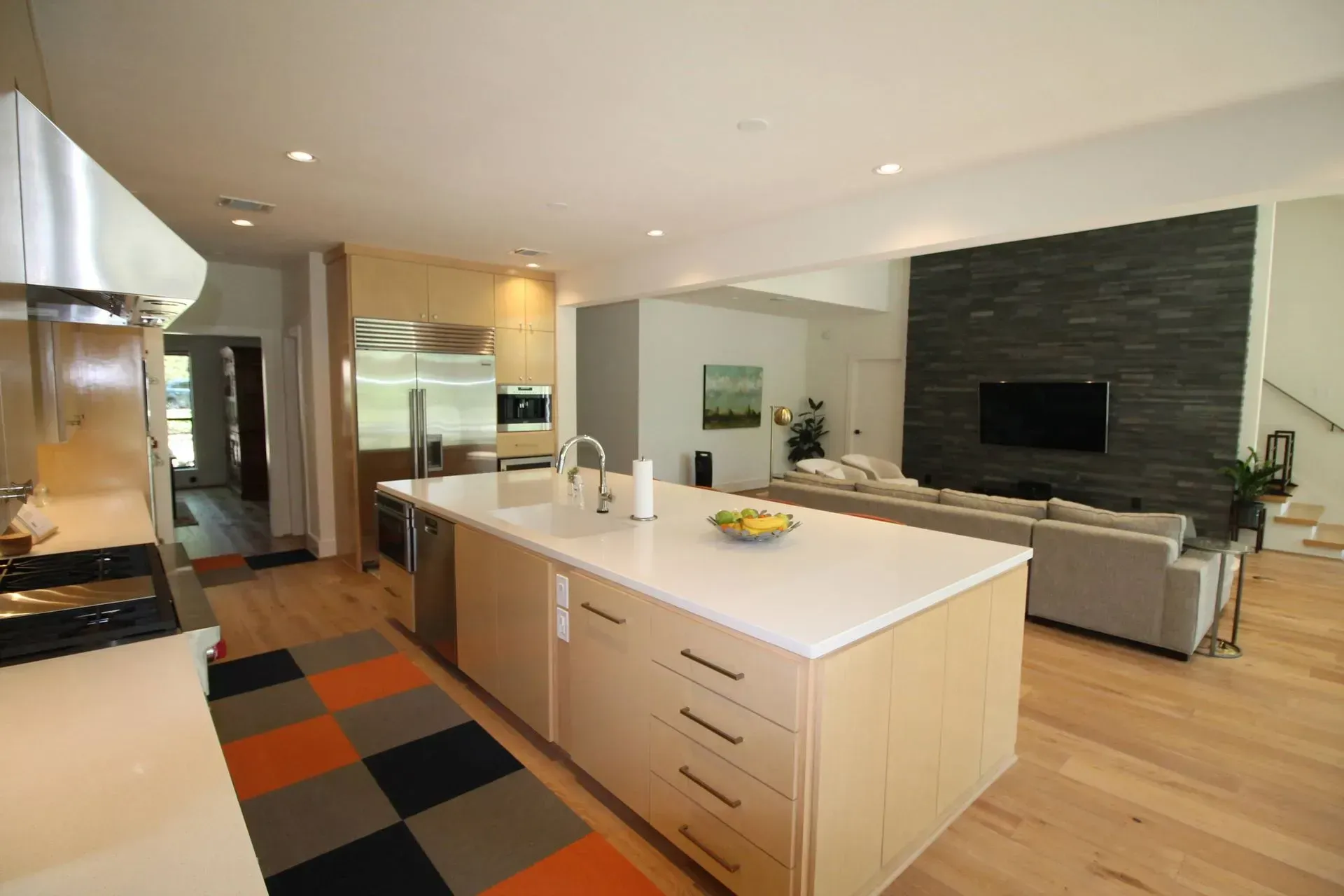 Modern open-concept kitchen and living room with island, wood floors, and dark stone fireplace wall.