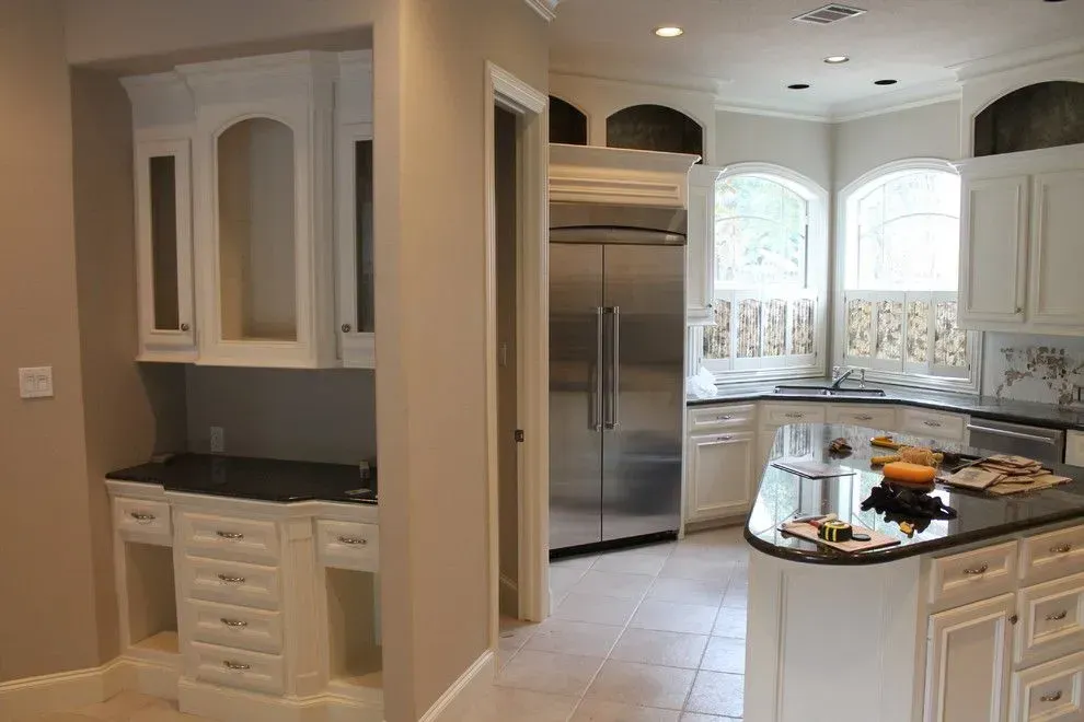 Elegant white kitchen with black granite countertops, built-in cabinetry, stainless refrigerator, and tiled floor.