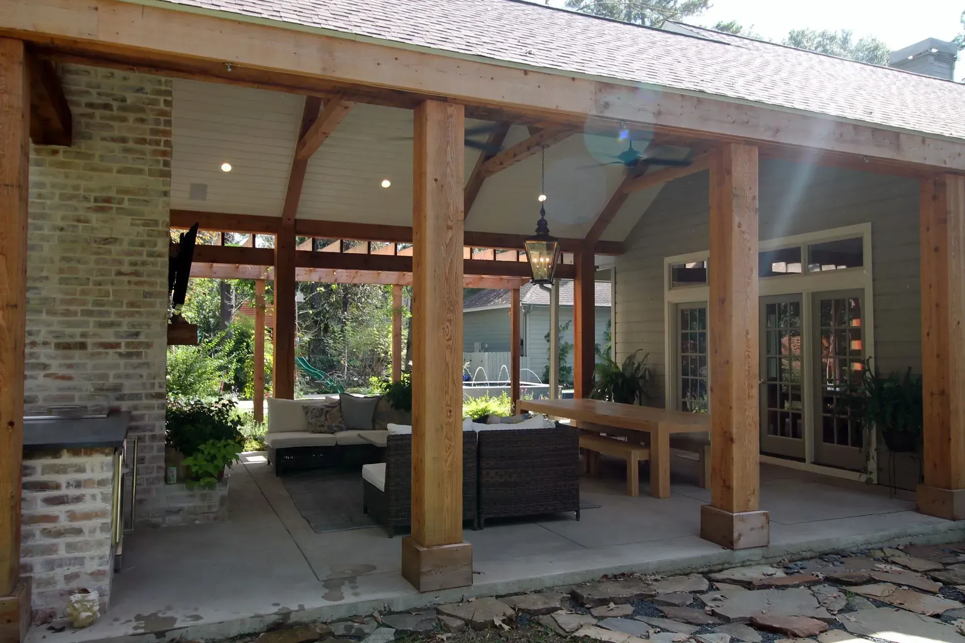 Covered patio with wooden beams, outdoor seating, and glass doors opening to a garden.