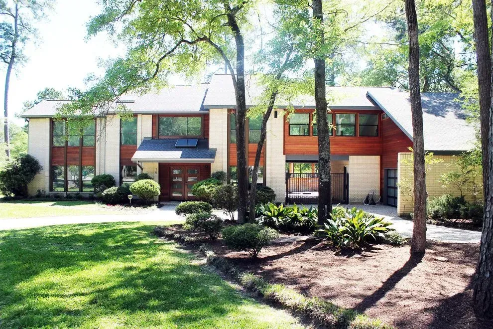 Two-story suburban house with tan siding, red shutters, and a landscaped front yard with trees.