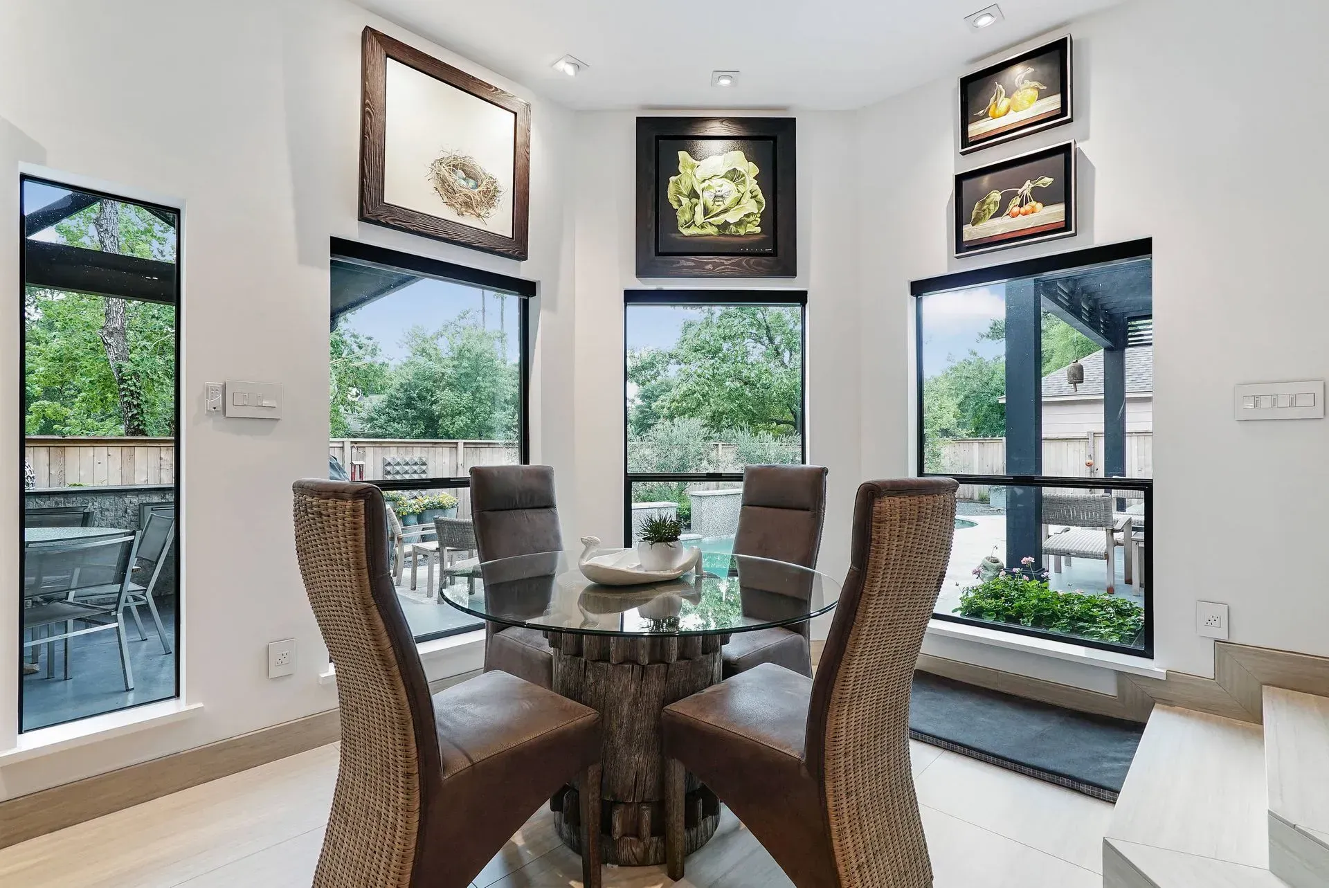Modern dining room with glass table, wicker chairs, and large windows overlooking greenery