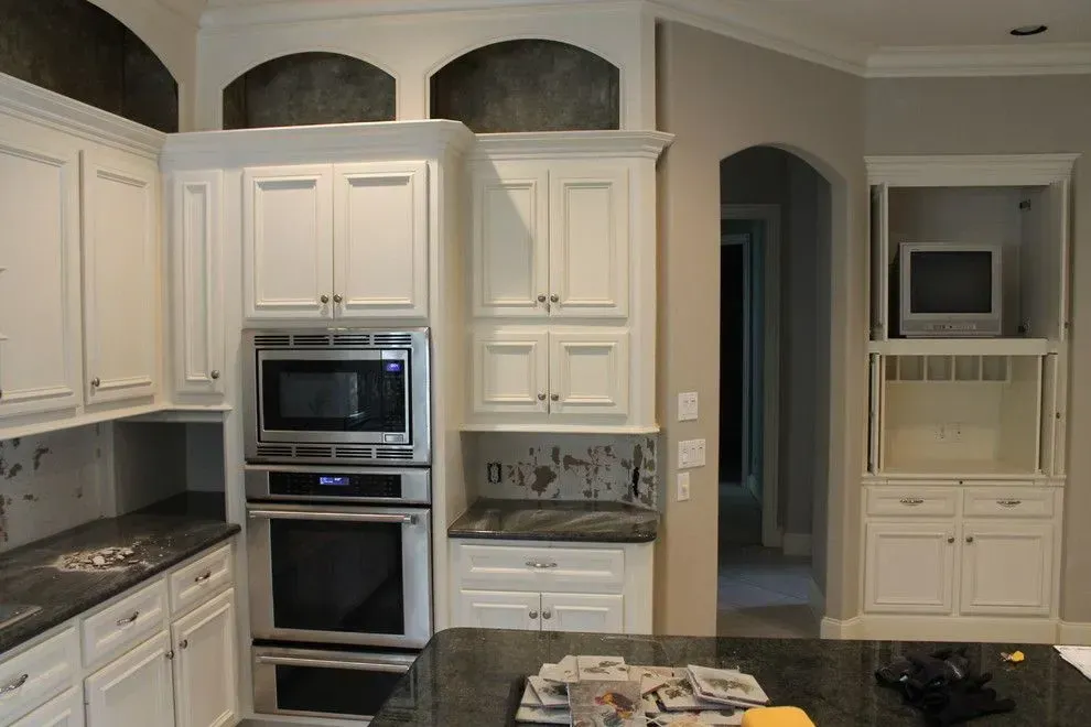 Bright kitchen with white cabinets, stainless steel oven, dark granite counters, and built-in microwave nook.