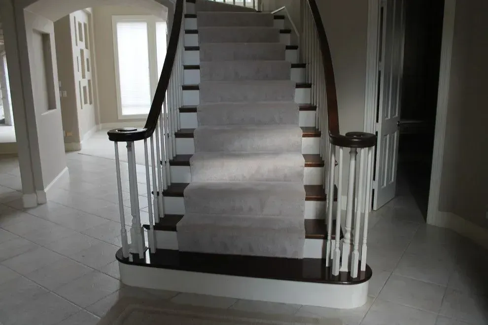 Curved staircase with white carpet runner and dark wood handrails in a tiled hallway