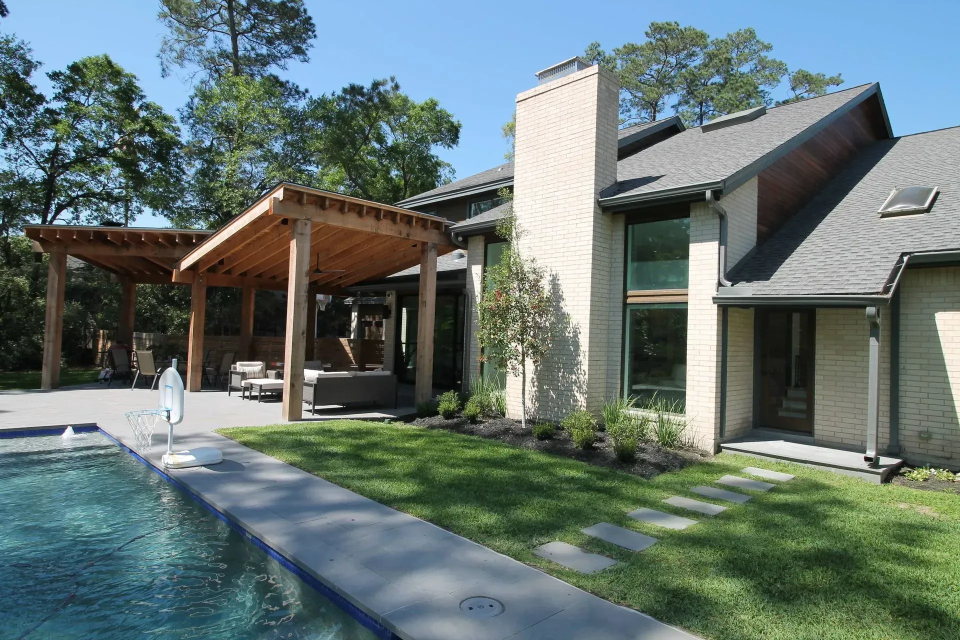 Modern house with a pool, patio pergola, and green lawn under a clear blue sky