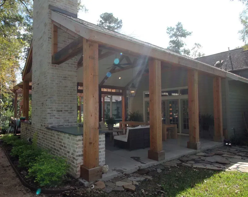 Outdoor patio with wooden pergola, brick wall, and stone walkway beside a house.