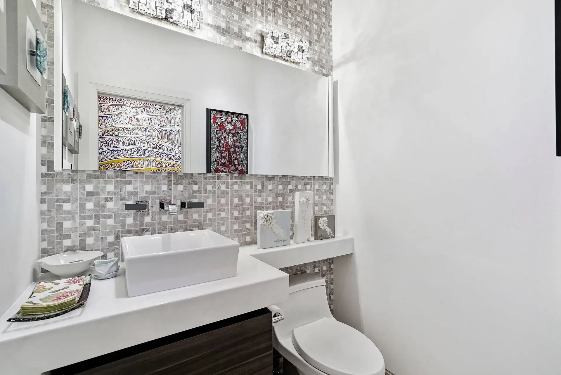 Modern bathroom vanity with large mirror, white sink, mosaic tile backsplash, and wall art