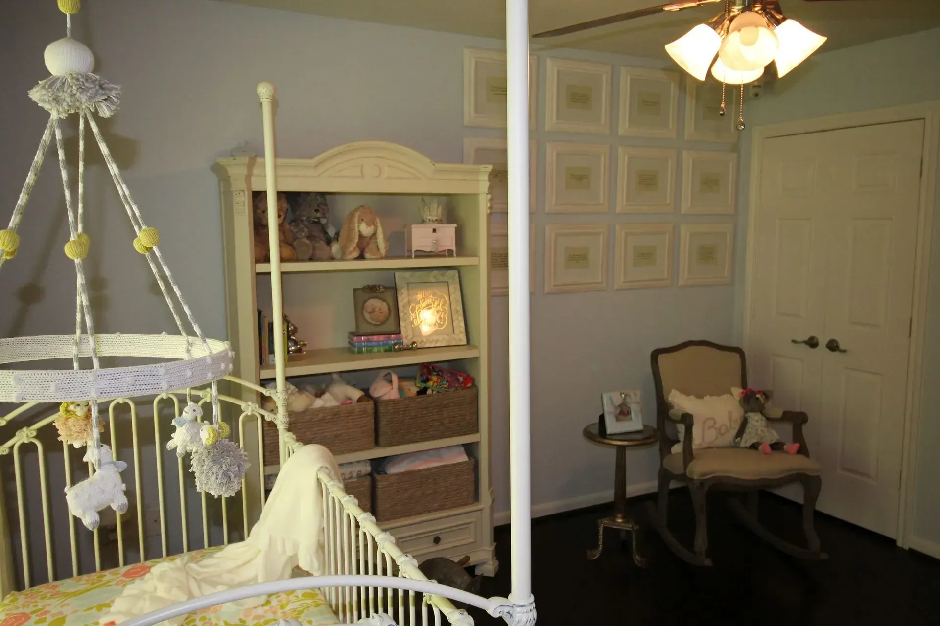 Pastel nursery with white crib, shelving, rocking chair, and framed wall art