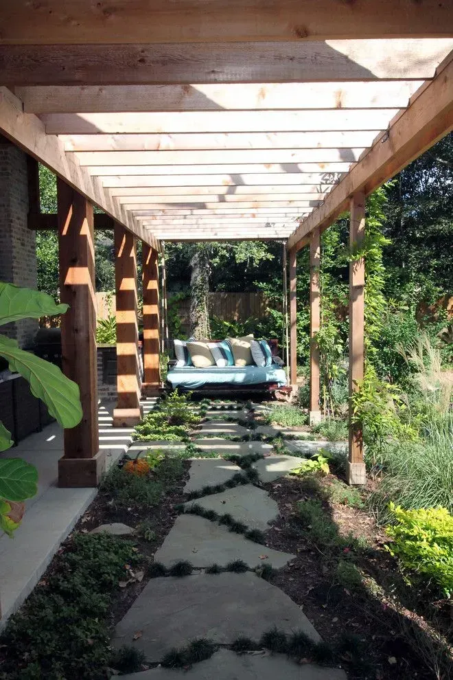 Wooden pergola over a stone path in a lush garden, leading to a blue bench in the background