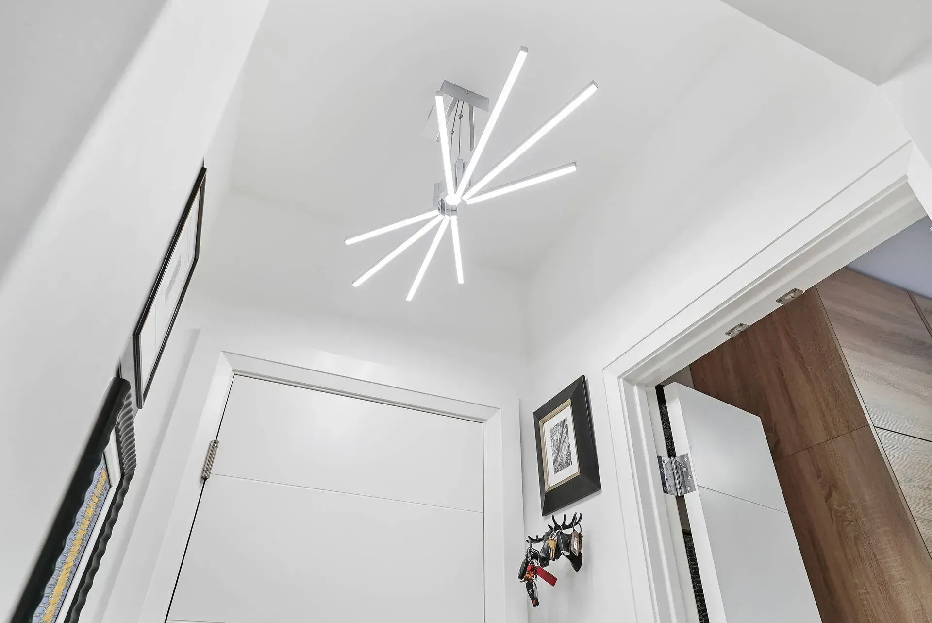 White hallway ceiling with a modern geometric light fixture, doorway, and framed wall art.