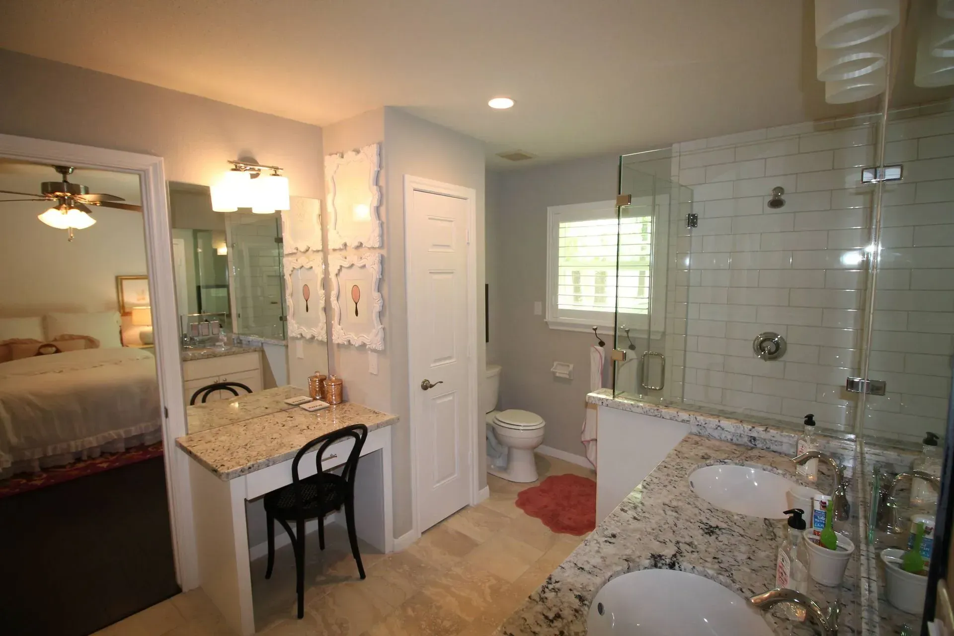 Bright bathroom with double sinks, large mirror, glass shower, and a bedroom visible through an open doorway
