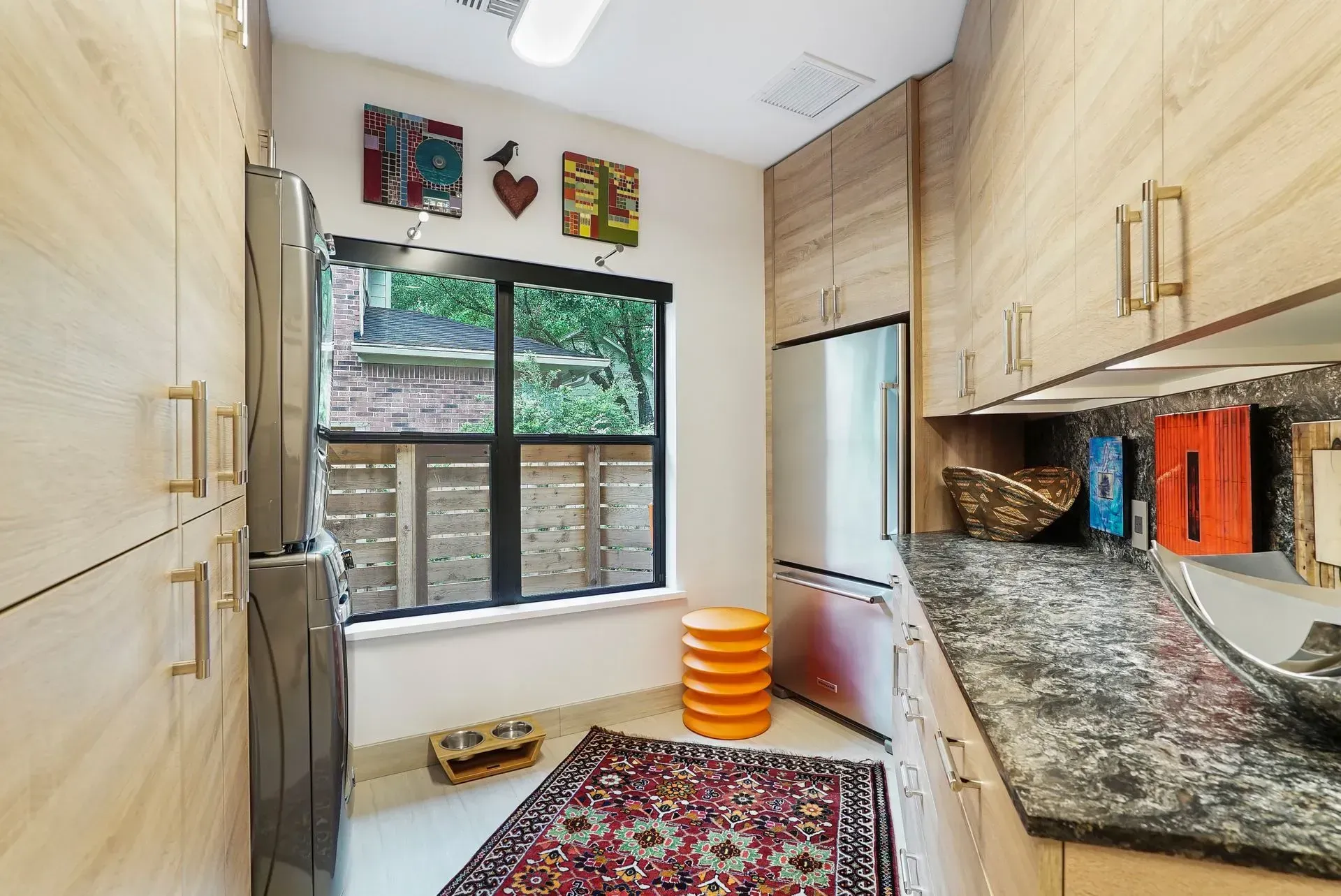 Bright laundry room with washer, dryer, window, cabinets, granite counter, and patterned rug