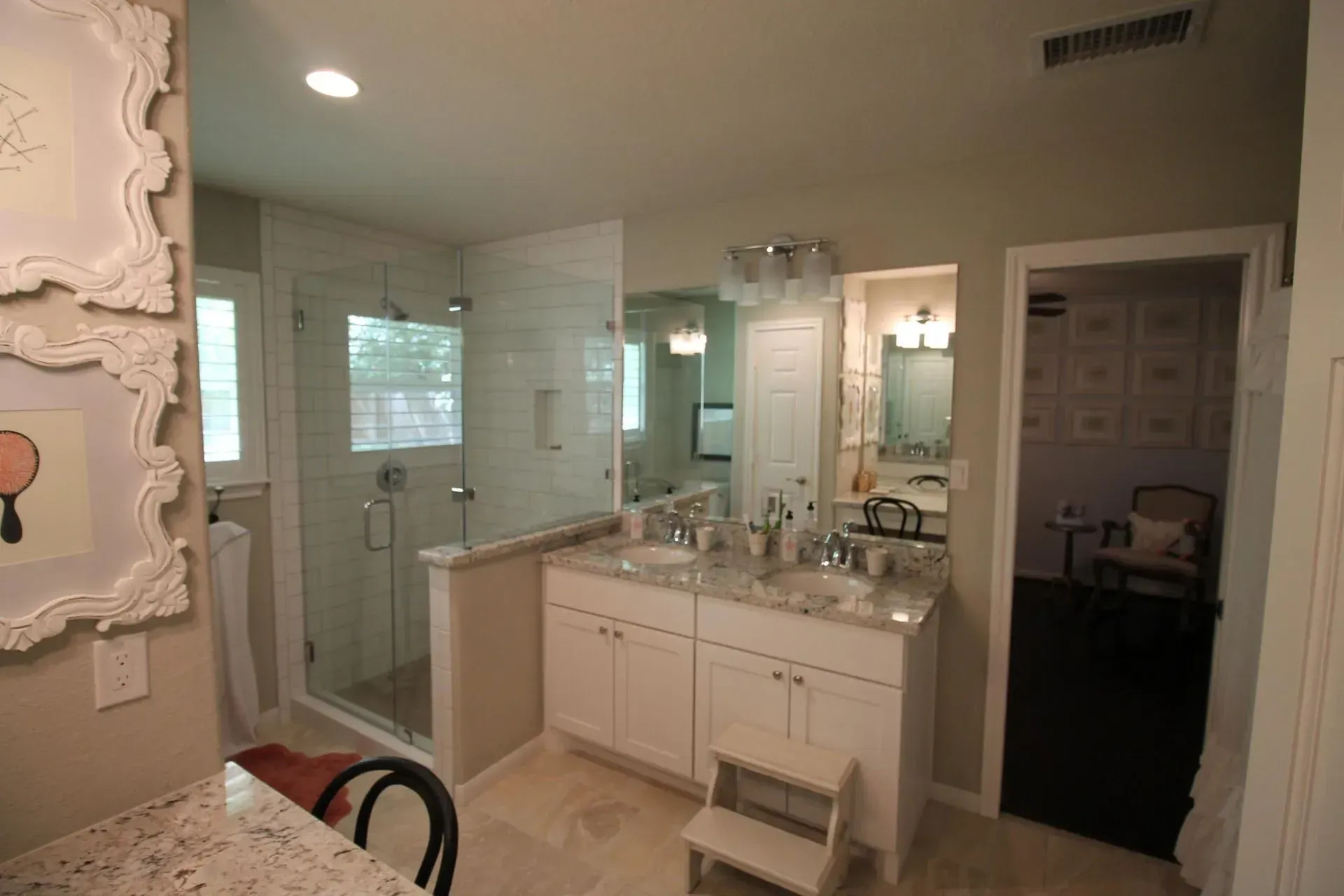 Bright bathroom with double vanity, large mirrors, glass shower, and white cabinetry.