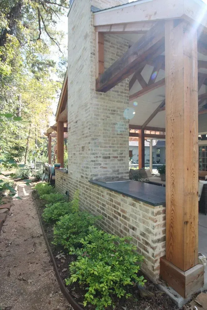 Brick-and-timber porch with large windows and greenery beside a wooded path