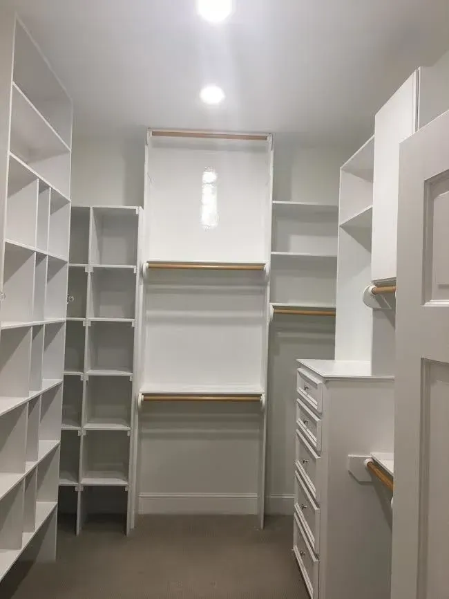 Walk-in closet with white built-in shelves, drawers, and hanging rods in a narrow, carpeted room