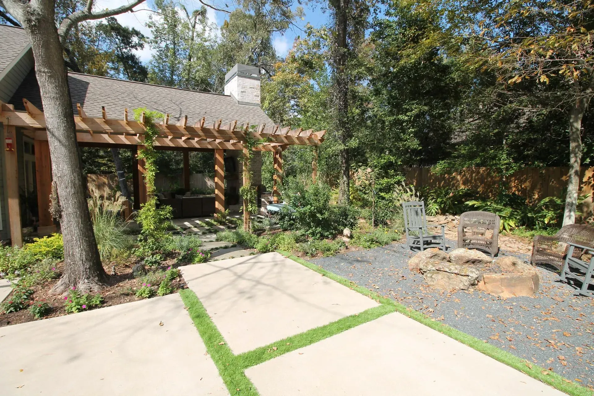 Courtyard garden with concrete path, trees, shrubs, and a building with a tiled roof