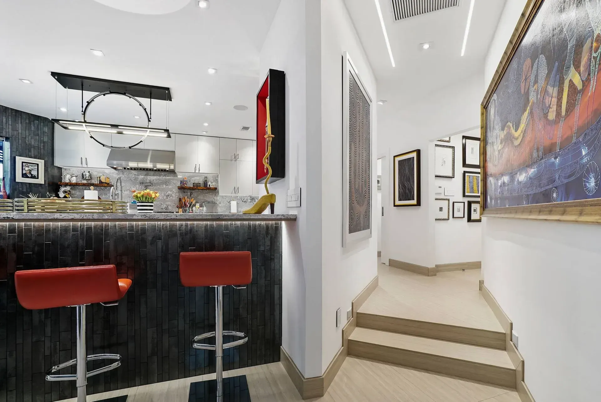 Modern gallery interior with a bar counter, red stools, and framed artwork along a bright hallway