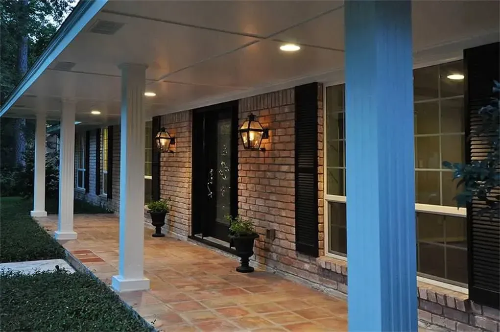 Covered brick walkway with white columns, lanterns, and windows along a building exterior