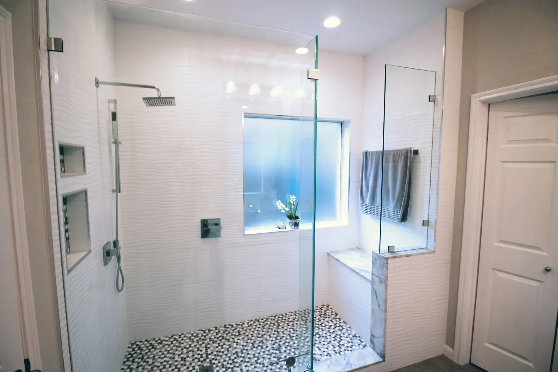 Modern white bathroom with glass shower, mosaic floor, vanity, and wall towel rack