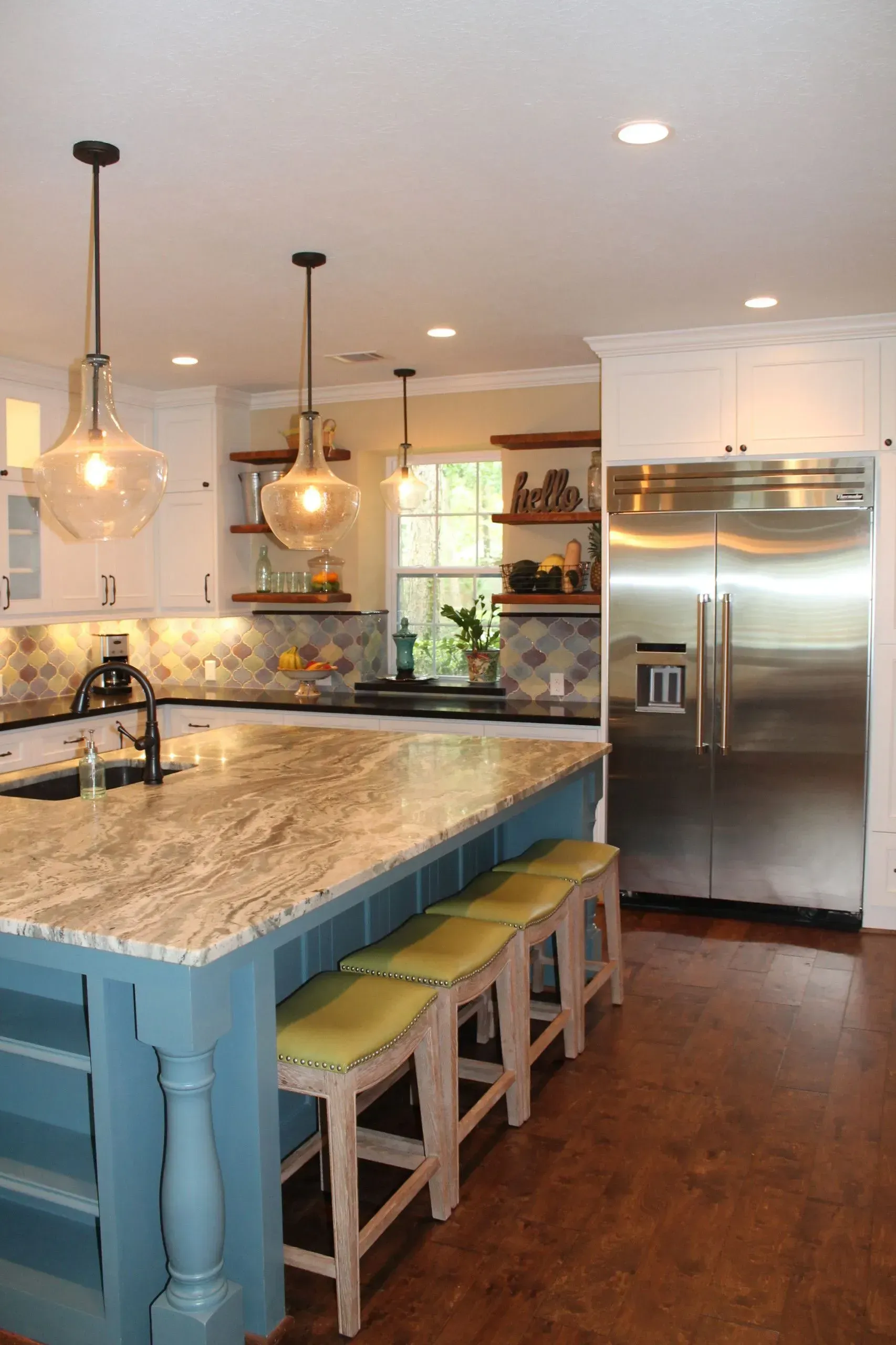 Modern kitchen with granite island, pendant lights, white cabinets, and stainless steel refrigerator