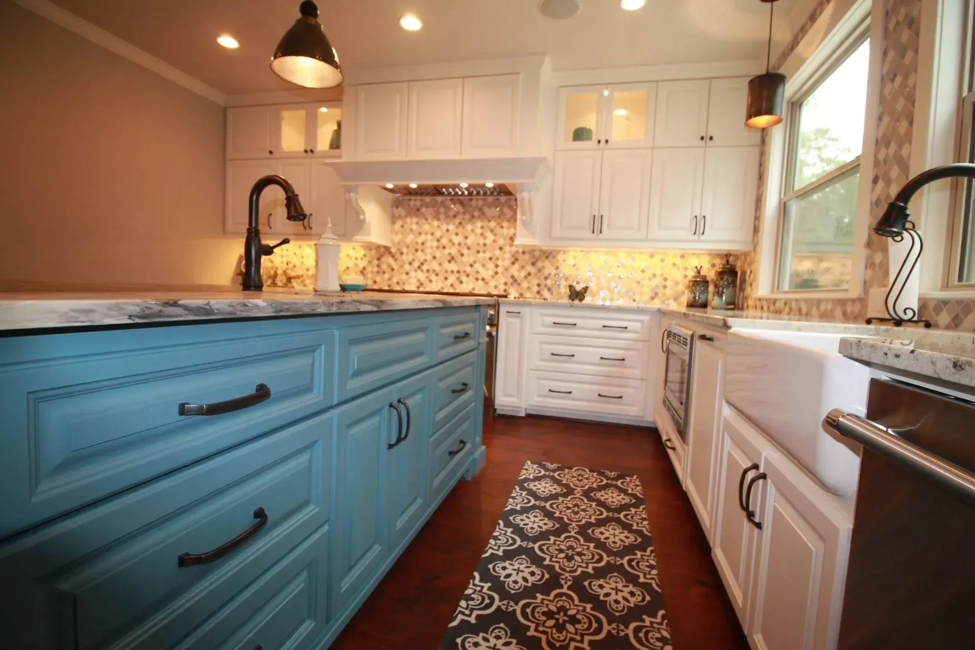 Bright kitchen with blue island, white cabinets, patterned rug, and pendant lights