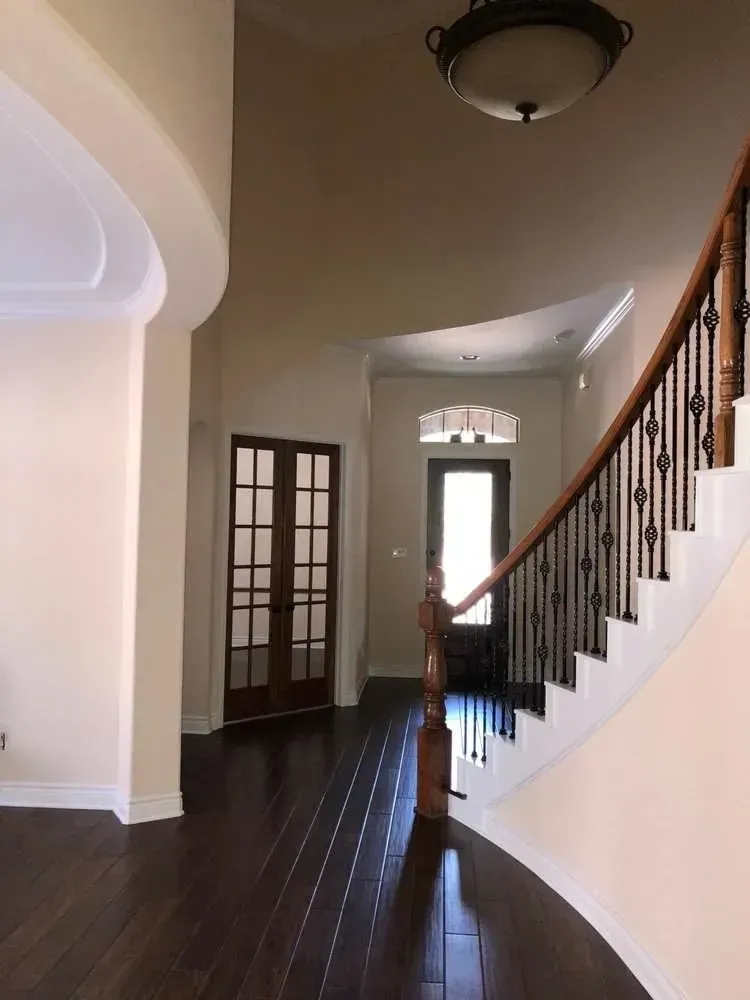Spacious foyer with dark hardwood floors, curved staircase, glass-paneled doors, and a ceiling light.