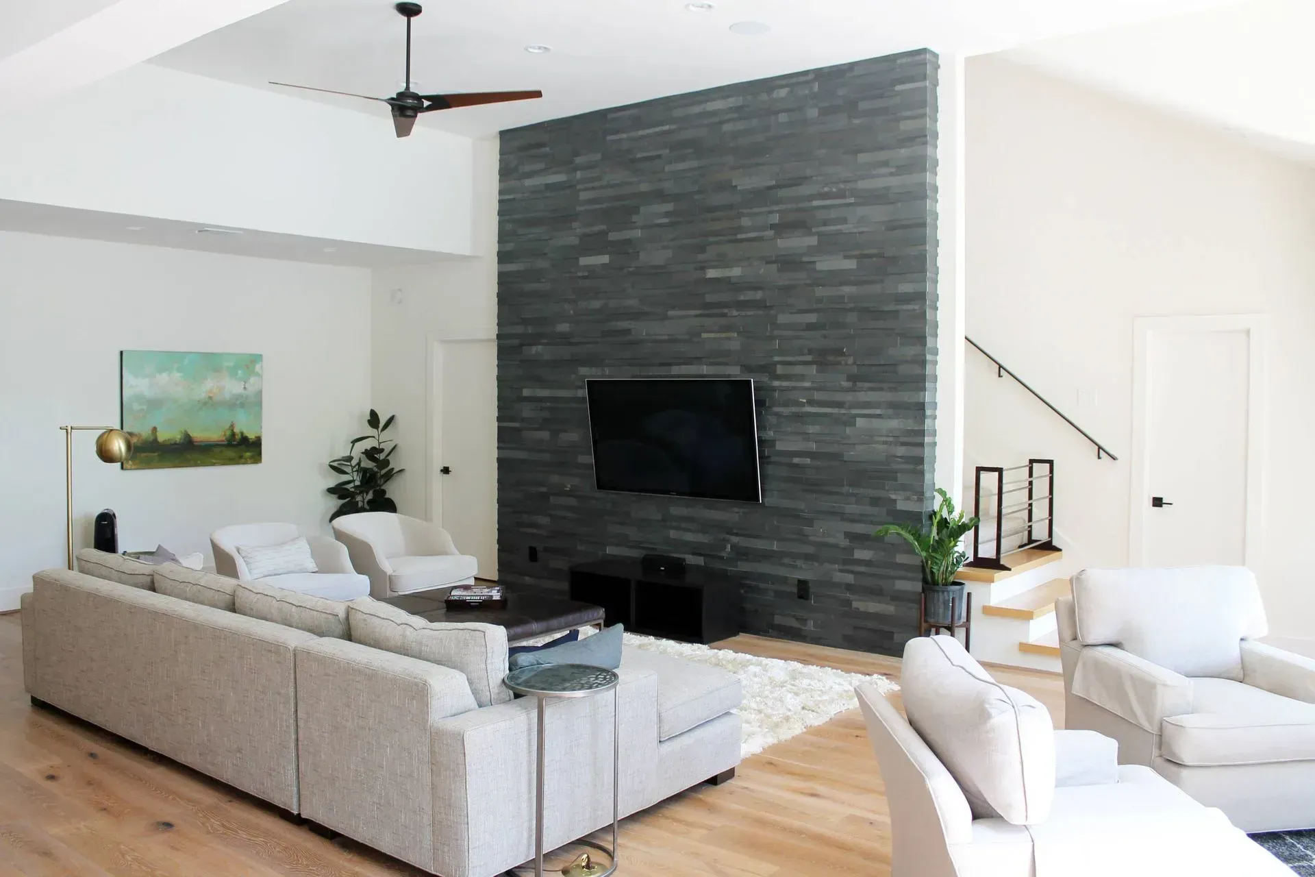 Bright modern living room with gray sectional, stone fireplace wall, and light wood floors