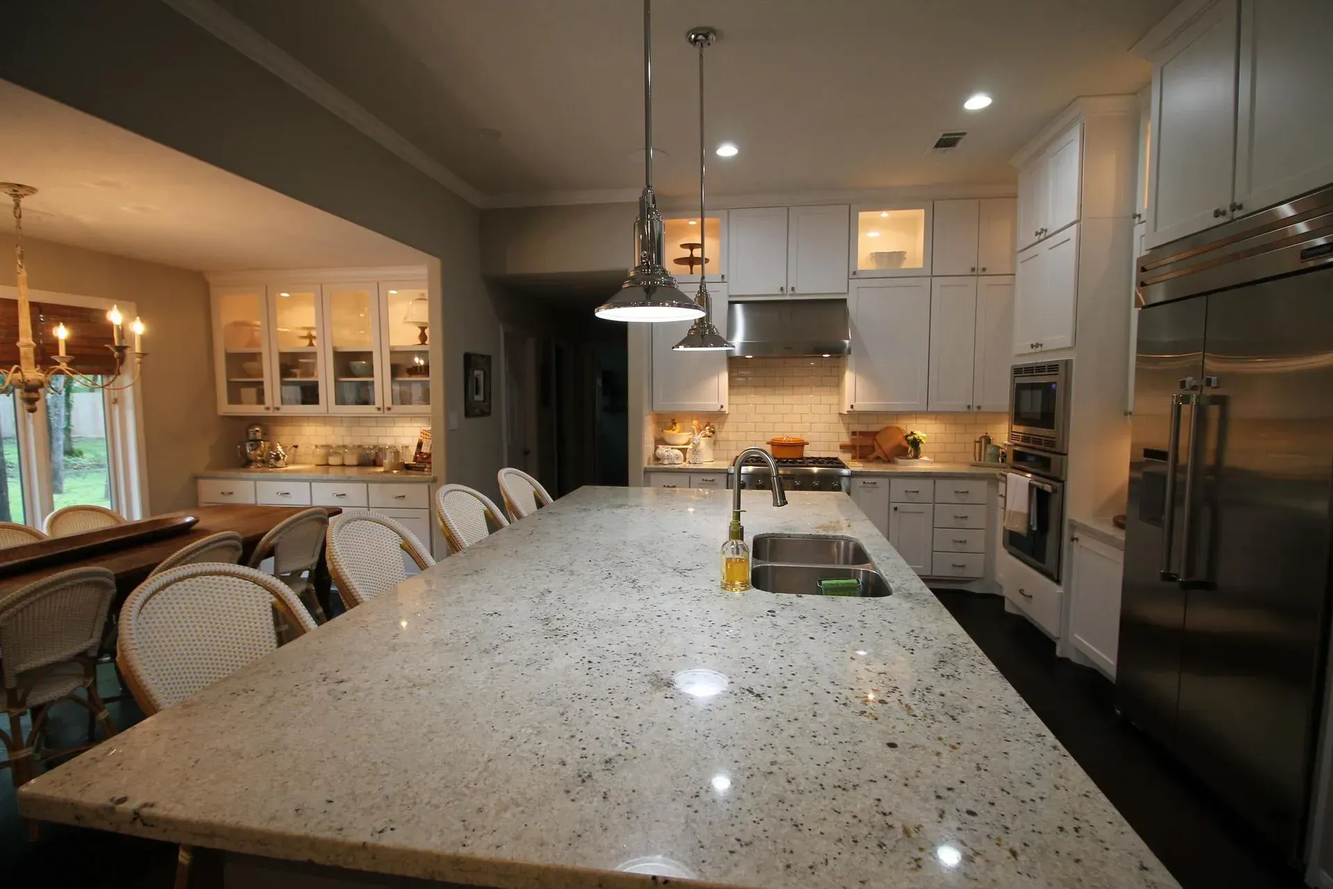 Modern kitchen with a large granite island, pendant lights, white cabinets, and stainless steel appliances