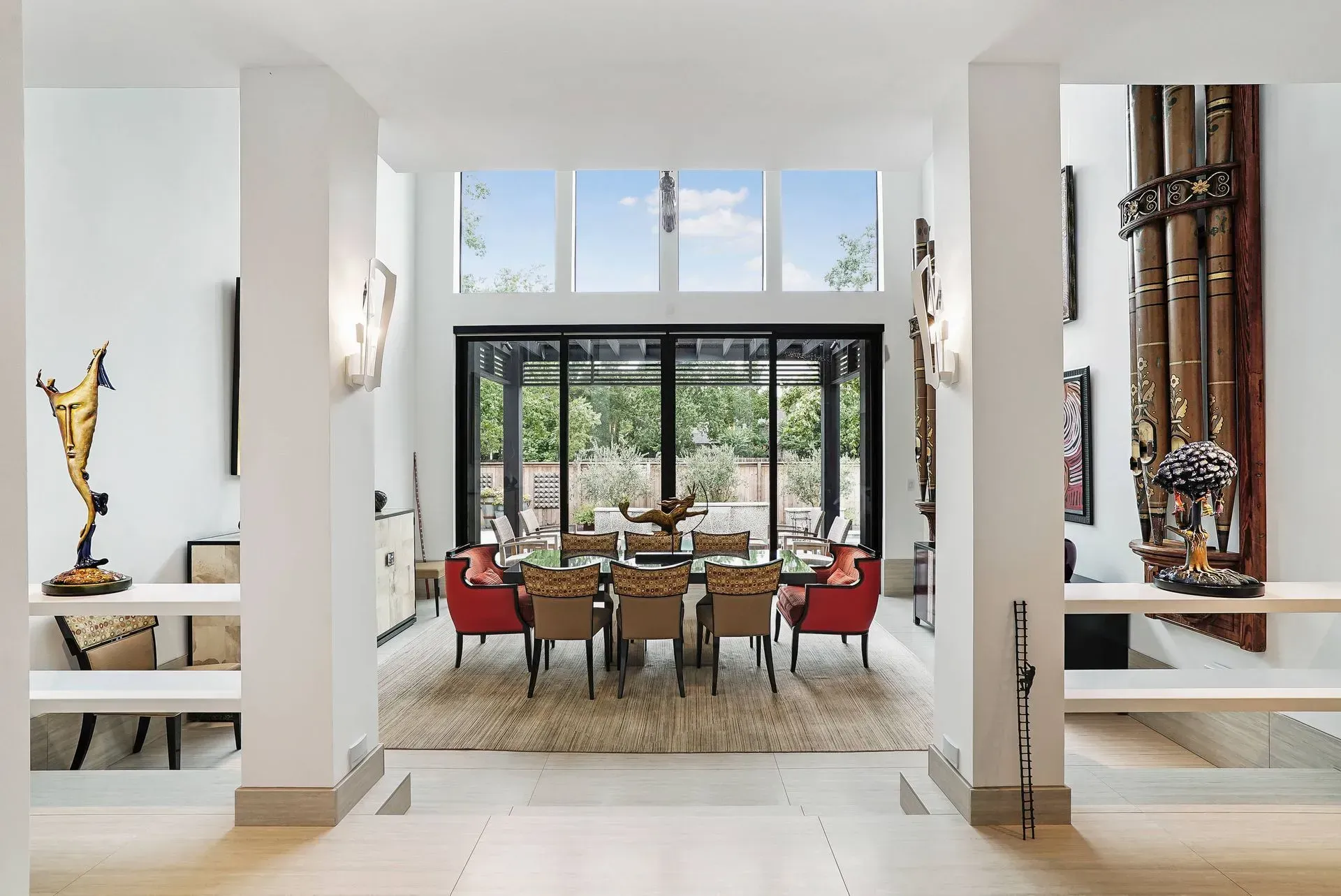 Bright modern dining room with black-framed windows, red chairs, and a table overlooking greenery