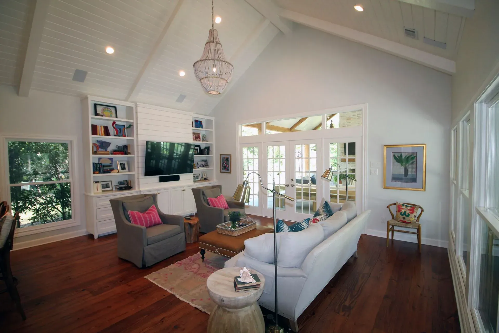Bright living room with white vaulted ceiling, gray and white sofas, wood floors, wall TV, and French doors.