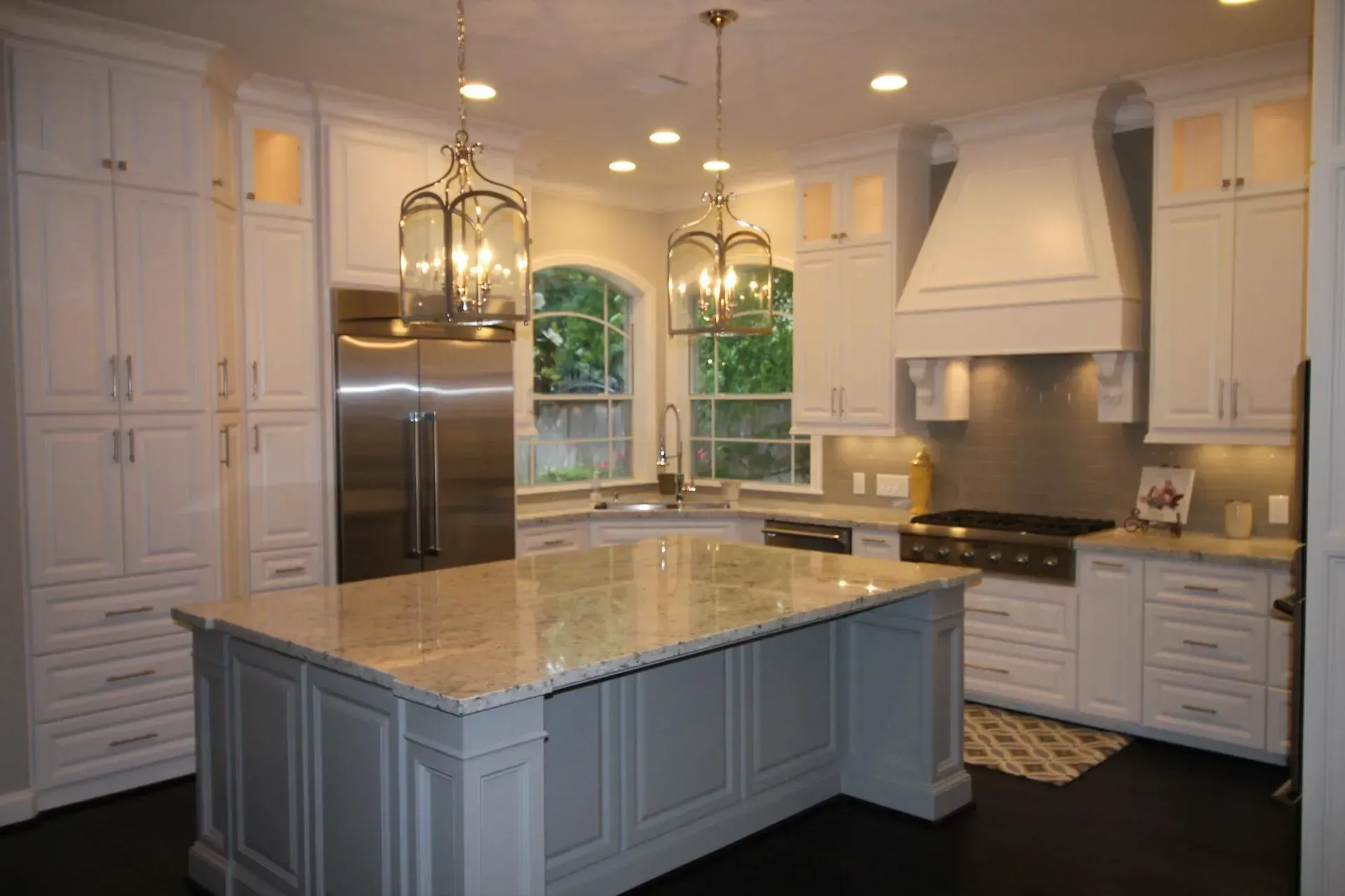 Bright modern kitchen with white cabinets, a large island, stainless steel fridge, and arched windows.