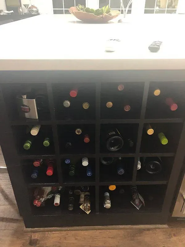 Black cubby wine rack filled with assorted wine bottles in a bright room