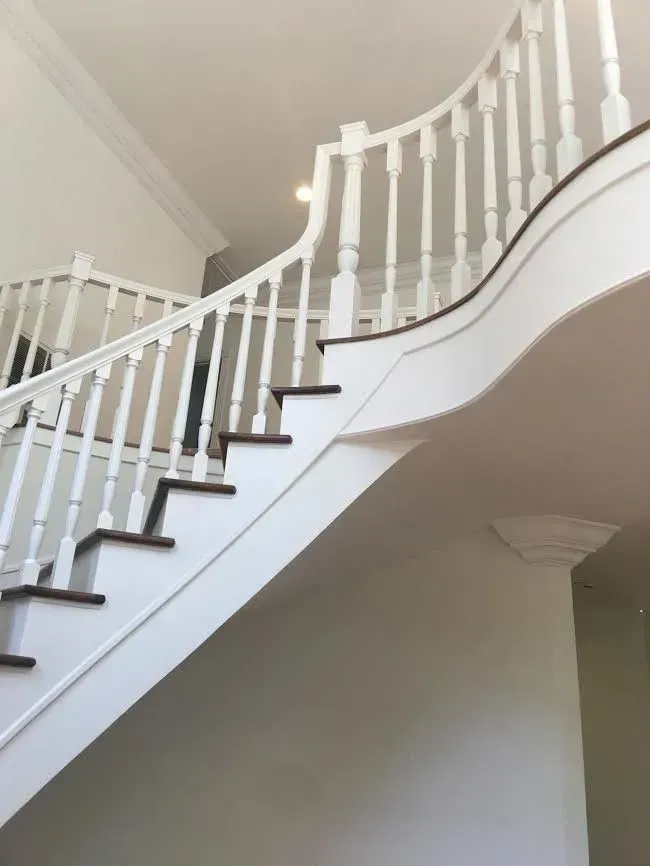 White curved staircase with dark wood steps and white railing in a bright interior.