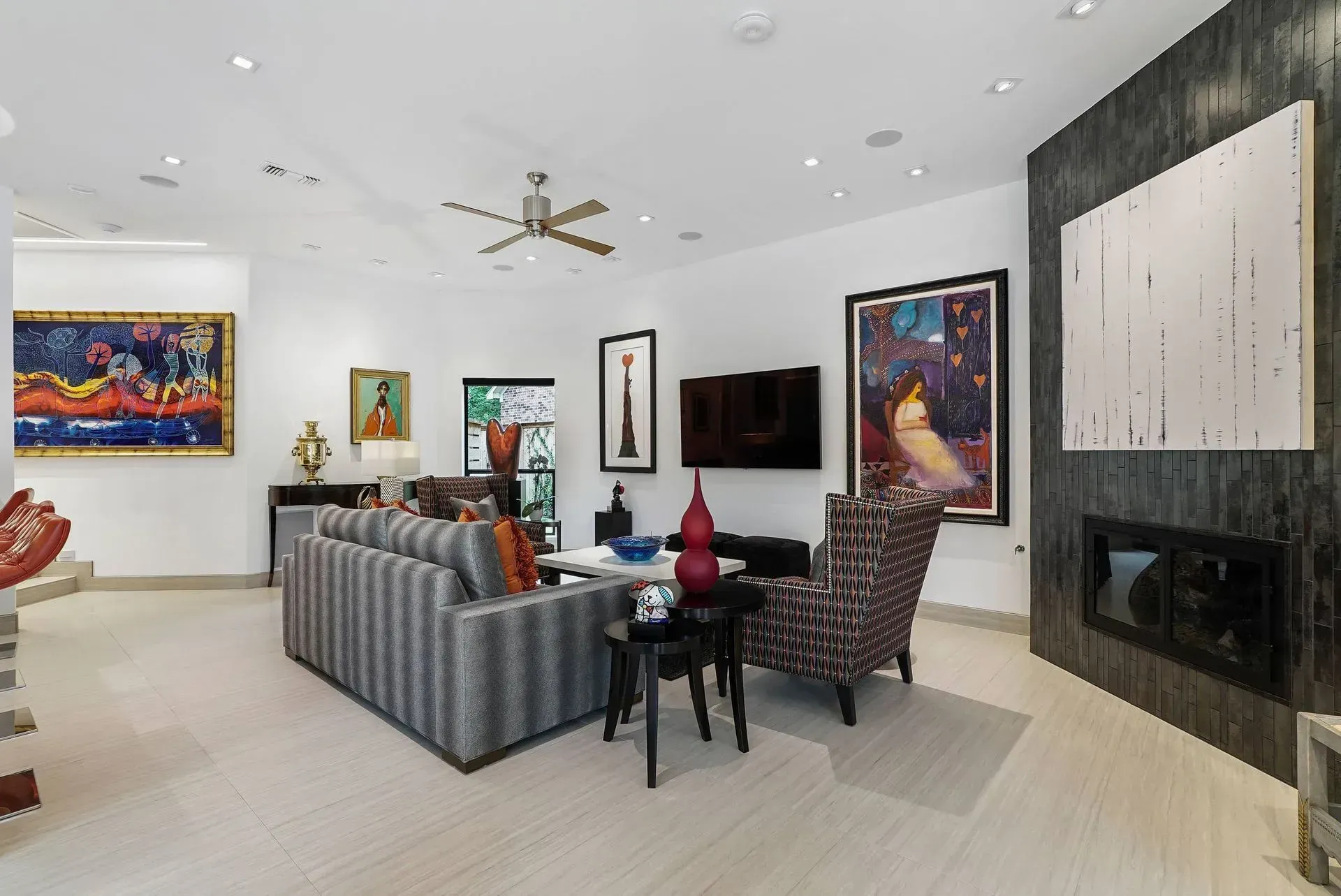 Modern living room with striped sofa, black fireplace wall, colorful artwork, and ceiling fan on white walls.