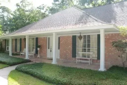 Brick house with white porch columns, green shrubs, and a covered front porch in daylight
