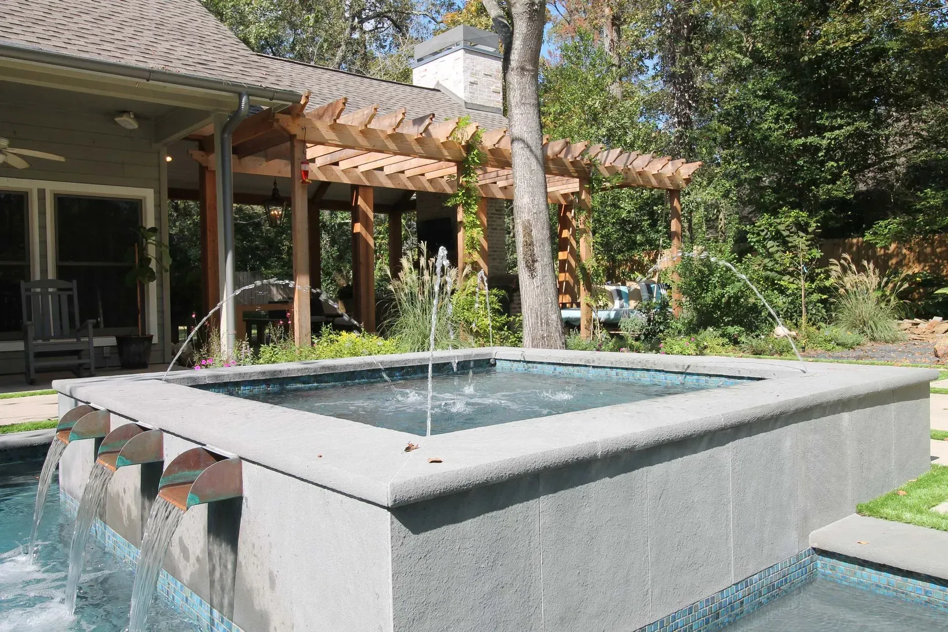 Modern backyard fountain with cascading water beside a covered patio and greenery