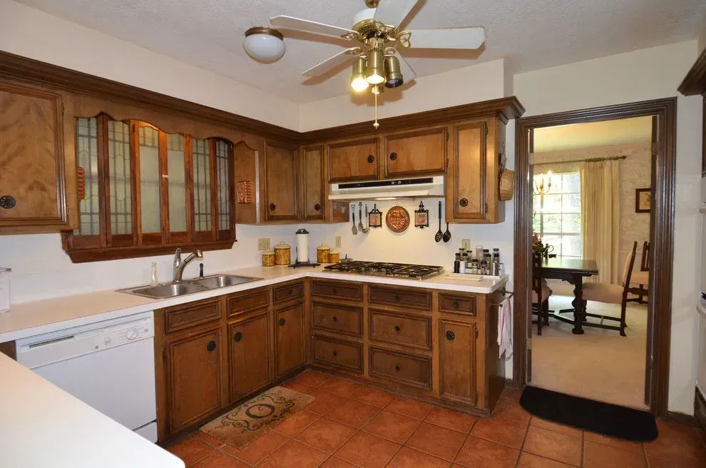 Wooden kitchen with white countertops, tile floor, ceiling fan, and a doorway to a dining room.